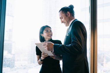 Modern ofisin penceresinin yanında duran ve tablet kullanırken projeyi tartışan çeşitli klas stil meslektaşlarından.