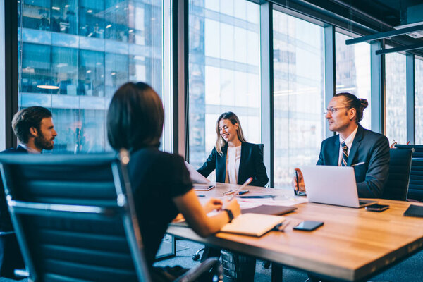 Процветающая команда финансовых экспертов в элегантной формальной одежде обсуждает бизнес-планирование в ходе продуктивного сотрудничества в фирме, успешные женщины и мужчины сотрудники консультируют о стартапе вместе