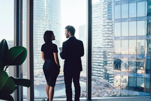 在当代工作场所 穿着华丽服装的男女同事站在窗边 讨论创业的想法 互相望着对方的背影 — 图库照片