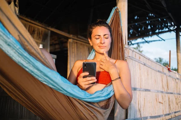 多愁善感的女性博主躺在摇摆式吊床上 沉思着网上出版的想法 沉思着的女性 带着现代智能手机小玩意 在旅游度假期间重新建立联系 — 图库照片