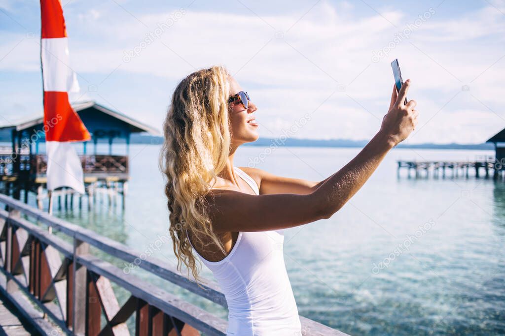 Cheerful female tourist using front camera for shooting influence video vlog about vacations in Thailand connecting to live streams on smartphone website, happy girl 20s making selfie pictures
