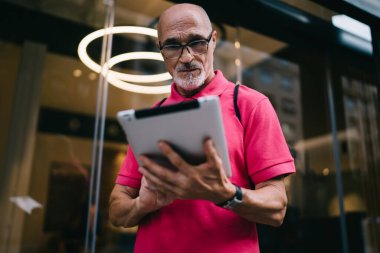 Şehirde boş zamanlarında kablosuz interneti taramak için dokunmatik ped kullanan yaşlı erkek blogcu, klasik göz giysisi giyen beyaz adam dijital tablette 4G 'ye bağlanan yayın haberleri okuyor
