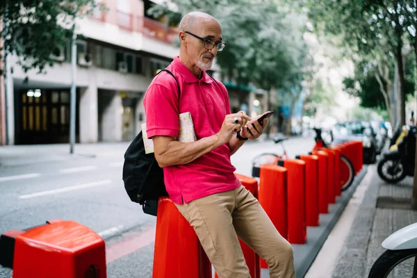 Mature male tourist connecting to 4g in roaming for using cellular application and make online booking, Caucasian man 60s in optical eyewear searching information via modern mobile device