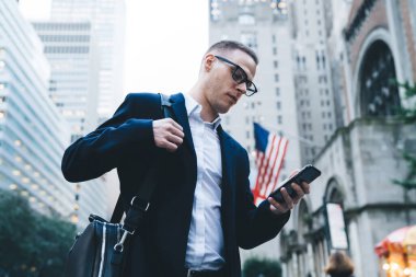 Palto giymiş ve çantalı akıllı telefonlu modaya uygun odaklı işadamlarından. Arka planda modern binalar olan caddede duran akıllı telefonlardan.