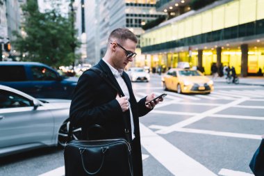 Gözlüklü ve ceketli, yaya geçidinin ve sosyal medyanın önünde duran kendinden emin ve zeki bir adamın yan görüntüsü