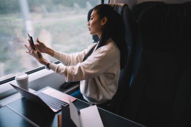 Akıllı telefon için poz veren Asyalı iş kadını, trende kablosuz bağlantıyla seyahat ederken, tren yolculuğu sırasında modern dijital cihazlar kullanan genç bir kadın.