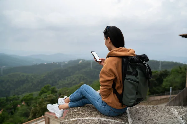 携帯電話で4Gを介してオンラインアジアの女性のシェアコンテンツの背面ビュー 空白の画面読み取り収入メールでスマートフォンを保持先保持中に休息バックパックと女性旅行者のバックパックのビュー — ストック写真