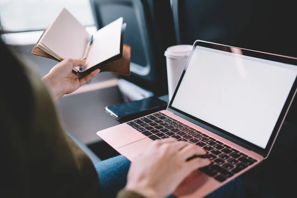 Cropped image of female author holding notebook and working remotely during journey sitting in train wagon, woman typing on laptop computer with mock up screen searching information on freelance job