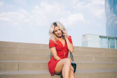 Çekici hippi kız kentte dinlenirken hücresel sohbetten hoşlanıyor, şık kırmızı elbiseli güzel kadın akıllı telefon cihazıyla tek başına seyahat etmek için dostça bir çağrı alıyor.