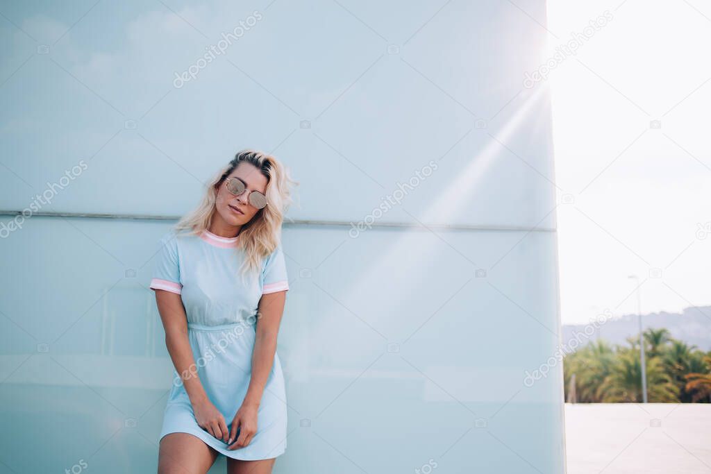 Half length portrait of trendy dressed hipster girl in fashionable sunglasses looking at camera during leisure at urbanity, youthful Caucasian model 20s posing during free time at city street