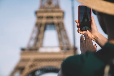 Paris 'in güneşli bir gününde Fransa' ya yolculuk sırasında ünlü Eyfel Kulesi 'nin dışını çekmek için akıllı telefon kullanan isimsiz bir kadın.