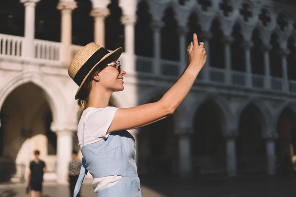 イタリアへの国際的な休暇を楽しんでヴェネツィアで晴れた日の間にコンテンツの写真をクリックして顔にかわいい笑顔を持つ幸せな女性 旅行ウェブサイトに影響を与えるために共有するためにビデオブログを撮影女性 — ストック写真