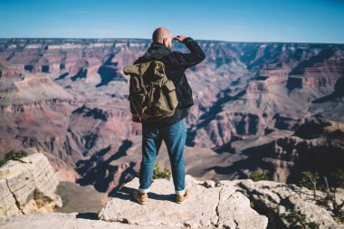 Sırt çantasıyla uçurumun kenarında duran ve Amerika 'daki Büyük Kanyon' un görkemli manzarasına hayran olan tanınmayacak kadar cesur bir adamın arka görüntüsü.