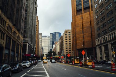 Amerika 'da New York' un işlek caddesinde gri gökyüzüne karşı modern yüksek binaların yanında asfalt yolda giden arabalar.
