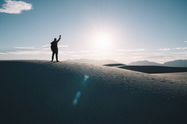 Gün batımında elleri kumlu çölde mavi gökyüzü ve arka planda yüksek tepeleri olan tanınmayan bir adam.