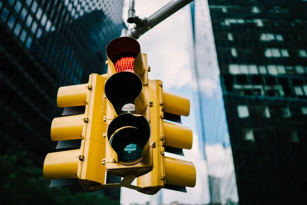 Low angle of yellow traffic light with red light with high tower and cloudy sky on background in New York City