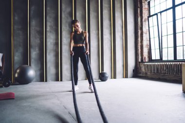 Aktif haldeki neşeli beyaz kadın kaslarını çalıştırmak için ip kullanıyor. Sağlıklı yaşam tarzının keyfini çıkarıyor. Mükemmel vücut hatlarını korumak için kameraya bakan güzel bir kadın.