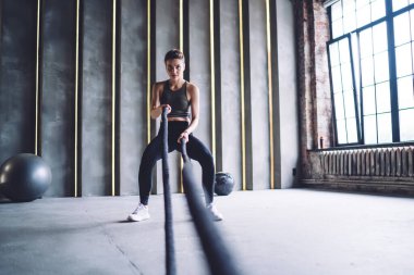 Hareketli beyaz kadın, spor salonunda zayıflatmak ve kol kasları üzerinde çalışmak için halat kullanıyor, ciddi trong profesyonel spor kadınları antrenman için sıkı kardiyo çalışması yapıyorlar.