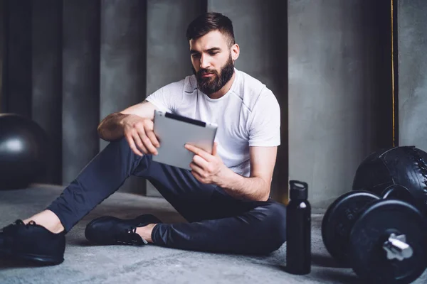 英俊的高加索胡子男性使用现代智能手机从社交网络中阅读信息 运动员在锻炼中检查手机在体操训练中的应用结果 — 图库照片