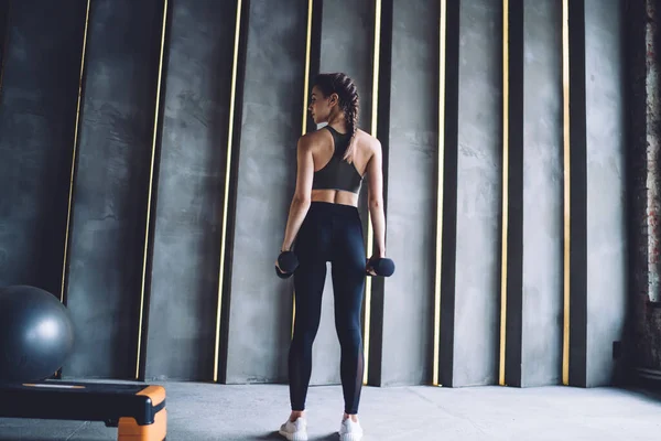 体育館でダンベルとトレーニングを開始する前に 黒の上とレギンスでスポーティな若い女性の完全な長さのバックビュー — ストック写真