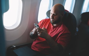 Ciddi hipster 'ın üstünkörü giyiminden, gemide internet kullanarak, telefonda mesajlaşarak, sosyal medyada uçarak, koltukta oturarak.