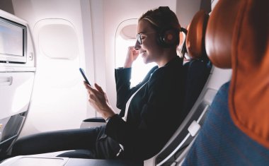 Yan bakışta gülümseyen kadın, kazanan jest ve yumruğunu sıkarken yolcu koltuğunda oturup cep telefonuyla müzik dinliyor.