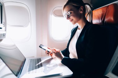 Düşük açılı, düşünceli, gözlüklü, zarif ceketli, akıllı telefonlu, netbook 'ta koltukta otururken ekrana odaklanan düşünceli yönetici kadın.