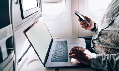 Uçuş sırasında ve uçağın penceresinin yanında otururken internet sayfası touchpad ve cep telefonu kullanan çiftçi erkeğin yan görünümü