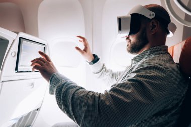 VR kulaklıklı, yolcu koltuğunda oturan ve uçuş sırasında sanal gerçeklikle etkileşim halinde olan bir erkeğin yan görüntüsü