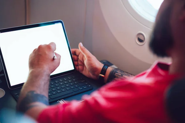 Side view of crop artful person in red t-shirt creatively drawing with stylus on laptop during flight wireless on board