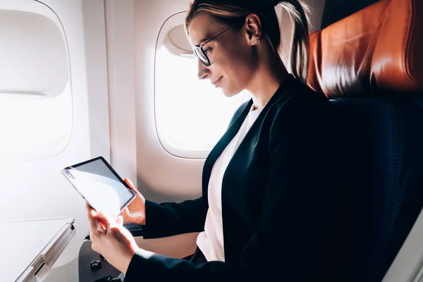 白种人女人戴著经典眼镜 在连接无线网络的现代触摸板上阅读有趣的电子书 成功的女性乘客在网上观看视频 — 图库照片