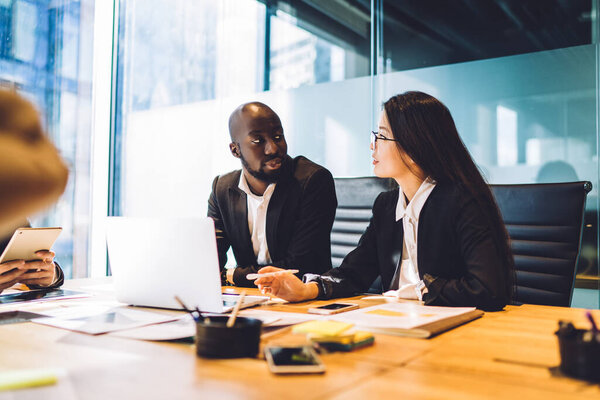 Diverse male and female colleagues discussing business exchange during working day in corporate company, skilled executive managers talking about web projecting analyzing together brainstorming