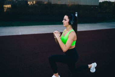 Kulaklık takan güçlü kararlı bayan sporcu vücut kaslarını çalıştırmaya ve fitness hedeflerine ulaşmaya odaklanmış. Vücut şekli mükemmel çekici bir kız dışarıda antreman yapıyor.