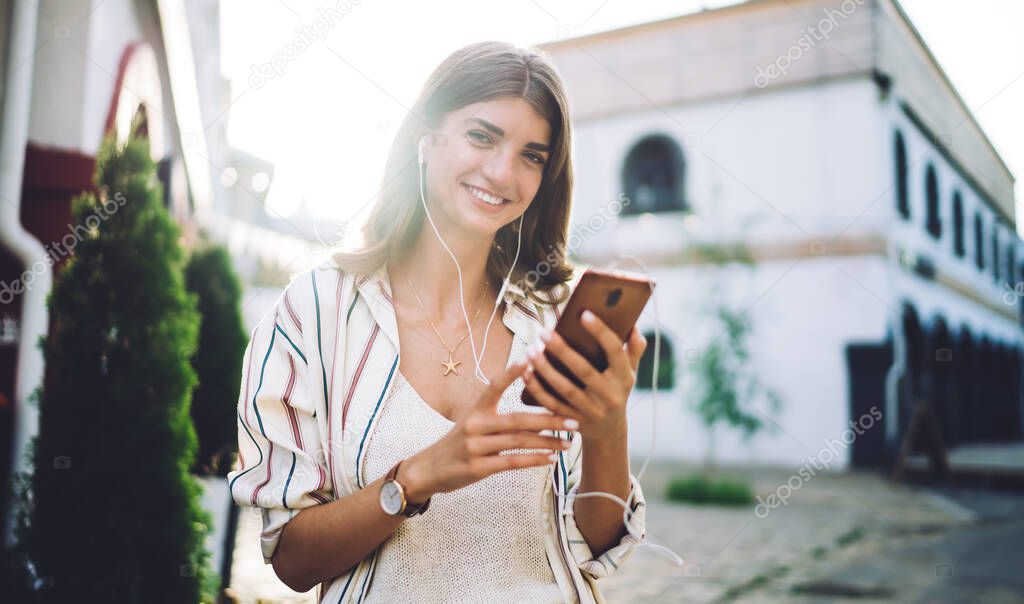 Half length portrait of happy woman in electronic equipment dialing contact number for communicate, cheerful hipster girl in earphones listening positive music podcast from smartphone application