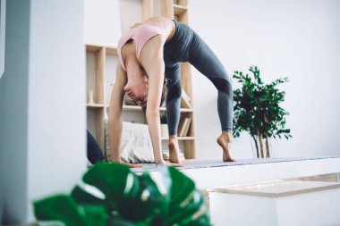 Düşük açılı, aktif giyimli genç sporcu kadın ışık odasında yerde yoga yaparken vücut eğilmesini gösteriyor.