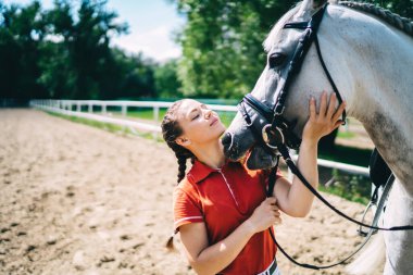 Beyaz giysili beyaz kadın sahibi, şirin beyaz atla boş zaman geçiriyor. Hafta sonunun tadını çıkarıyor. Favori hobisi, çiftlik çiftliğinde hayvanlarla ilgilenen genç kadın jokey.