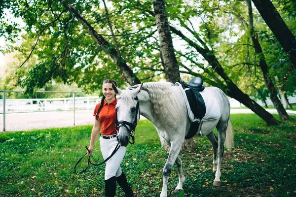 穿着骑师靴和休闲装的快乐的职业女性骑着纯种马在公园里散步 看着镜头 — 图库照片