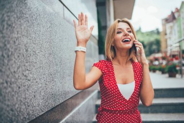 Yüzünde sevimli bir gülümseme olan modaya uygun giyinmiş bir kadın cep telefonu aygıtı kullanarak gezintiye çıkıyor, telefon ediyor ve buluşma saatinden bahsediyor, mutlu kız sokakta el sallıyor ve arkadaşça cep telefonu sohbetinden keyif alıyor.