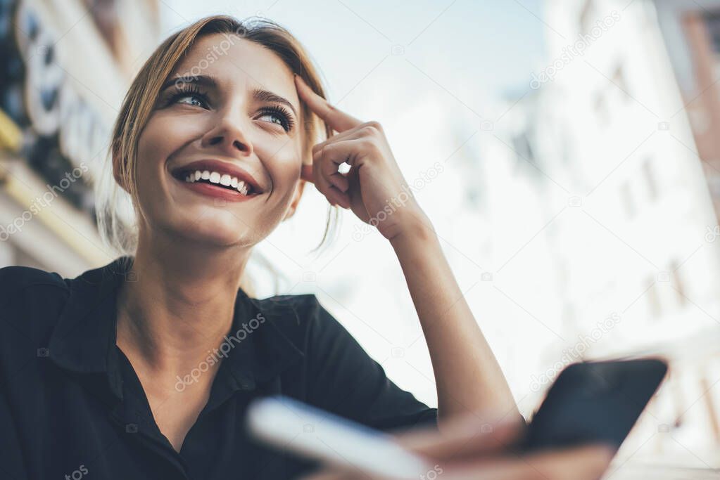 Cheerful Caucasian woman with candid smile on face feeling happiness during smartphone networking for web socialising with followers, prosperous hipster girl with white teeth using cellular technology