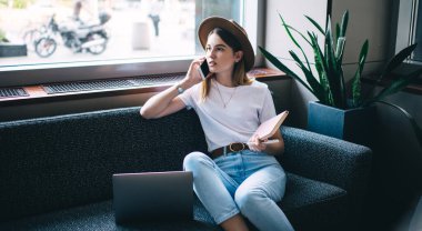 Ciddi, 20 'li yaşlarda, modaya uygun şapkalı, serbest iş üzerine cep telefonu sohbetine odaklanmış beyaz kadın, cep telefonu operatörüne cep telefonu aracılığıyla çağrı yapan,