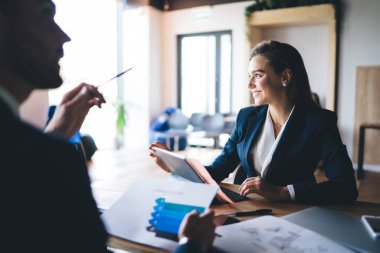 Resmi olarak dizüstü bilgisayarı olan mutlu genç iş kadınının yandan görünüşü, güneşli bir günde modern ofis çalışma alanındaki iş arkadaşlarıyla iş stratejisi hakkında konuşurken başka yöne bakıyor.