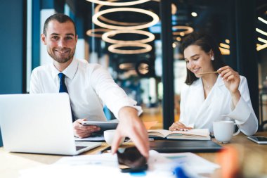 Neşeli başarılı meslektaşlar, notlarda notlar, tabletlerde belgeler ve kahve içerken masada birlikte oturuyorlar.