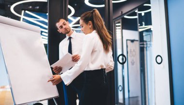 Dikdörtgen çizelgeye yakın duran ve modern ofiste erkek genel müdürün denetimi altında iş stratejisi düşünen konsantre kadın işçilere yan bakış.