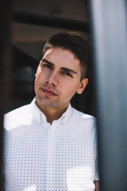 Düşünceli bir adam gündelik giysiler içinde şehrin modern binasının yakınındaki kameraya bakıyor ve hafta sonu boyunca düşünceli bir şekilde bakıyor.