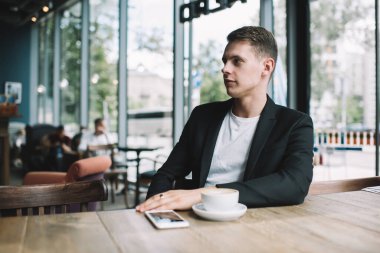 Karizmatik genç adam rahat bir kafede dinleniyor. Bir fincan kapuçinoyla gündüz gözünü kaçırıyor.