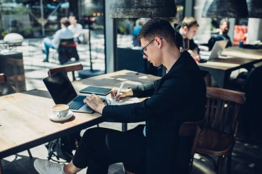 Gündüz vakti modern kafe projesinde çalışırken not yazan ve dizüstü bilgisayar kullanan genç işadamlarının yan görünümü