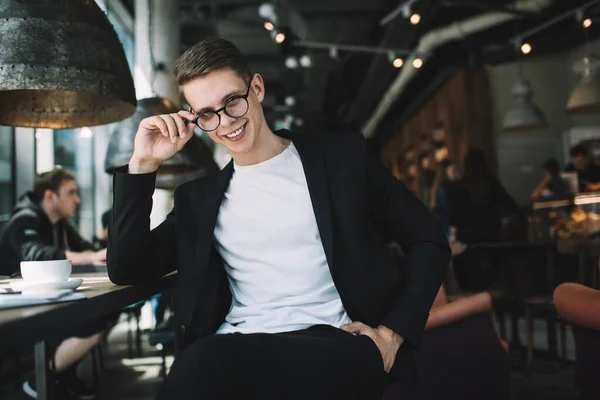 Satisfied Youthful Male Formal Clothes Touching Eyeglasses Smiling While Sitting — Stock Photo, Image