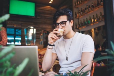 Kafkas erkek serbest görüşlü, vizyon koruması için gözlüklü, internetten video izlerken kahve içen, kafein içen ciddi bir hippi. İnternet kursu eğitimi için internet sayfası.