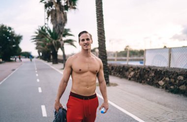 Suyla antrenman yaptıktan sonra caddede duran kaslı seksi gövdeli, gülümseyen beyaz hipsterin yarım boy portresi. Beyaz tenli güçlü sporcu antrenmandan zevk alıyor ve mükemmel vücut şeklini koruyor.