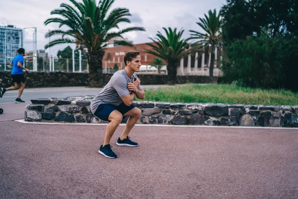 Determined sportsman squatting on street workout looking weight and recreating on active healthy lifestyle routine in morning, male athlete in active clothes exercising and training muscular body